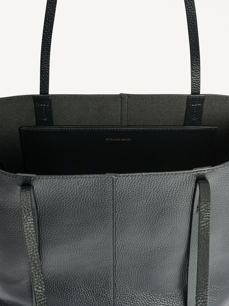 By Malene Birger Abilso veske i sort, strukturert skinn, med tote-form, liten logo i front og lange bærereimer.
