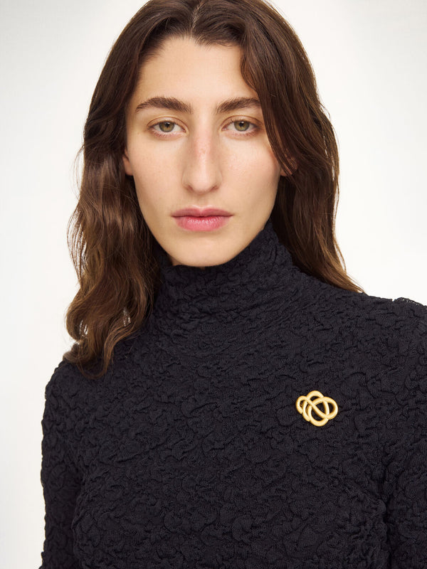 By Malene Birger Broche mini brosje i gullfarget sink, med myke linjer og et tidløst Swirl-motiv.