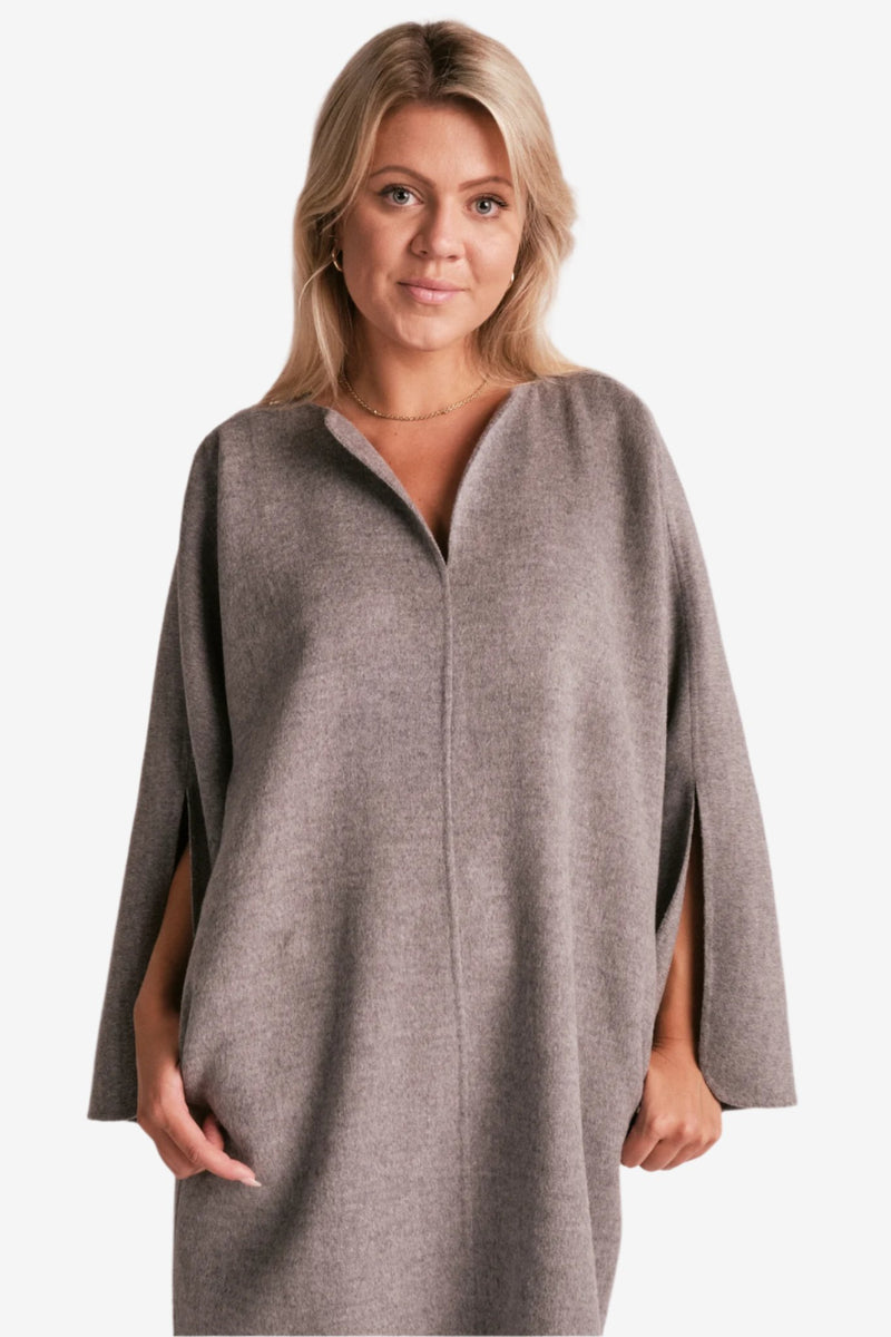 By Malene Birger Cais kjole i grått, laget av 100% ull, med en løs passform, v-utringning og splitt på ermene.