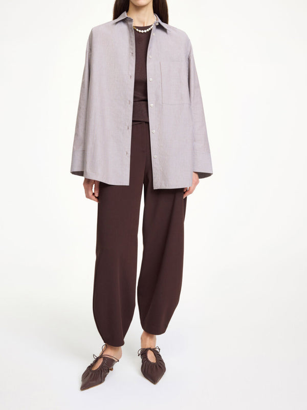 By Malene Birger Derris bomullskjorte i brun- og hvitstripet organisk bomull, med en oversized passform og brystlomme.