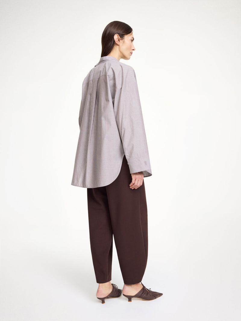 By Malene Birger Derris bomullskjorte i brun- og hvitstripet organisk bomull, med en oversized passform og brystlomme.
