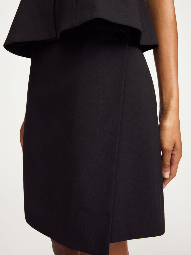 By Malene Birger Esma omslagsskjørt i sort, laget av resirkulert polyester, viskose og elastan, med en knapp i siden.