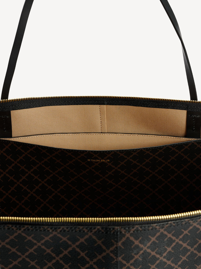 By Malene Birger Luze veske i mørkebrun, med Signature Flower-mønster, glidelåslukking og smale stropper.
