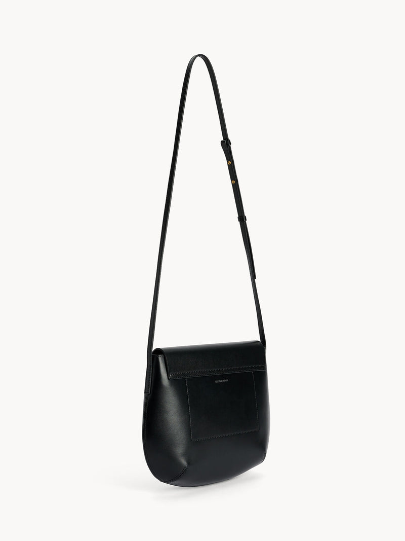 By Malene Birger Maellon veske i blankt, sort kuskinn, med diskret monogram i front og justerbar stropp.

