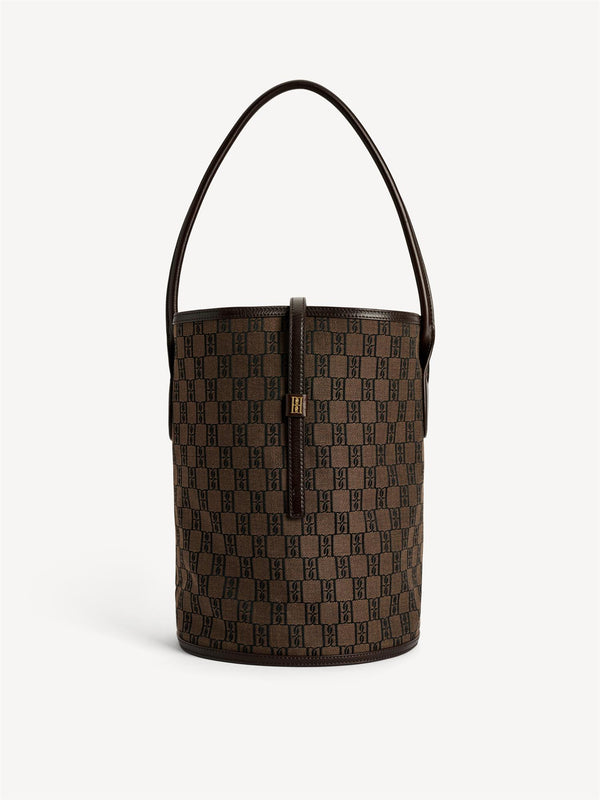 By Malene Birger Maryllon veske i brun, med bøtteform, laget av resirkulert bomull og polyester, og et gullfarget monogram-emblem i front.