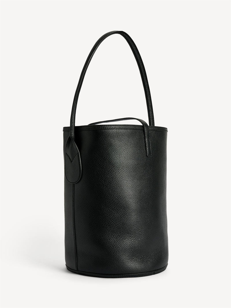 By Malene Birger Maryllon veske i sort skinn, med bøtteform og gullfarget monogram-emblem i front.