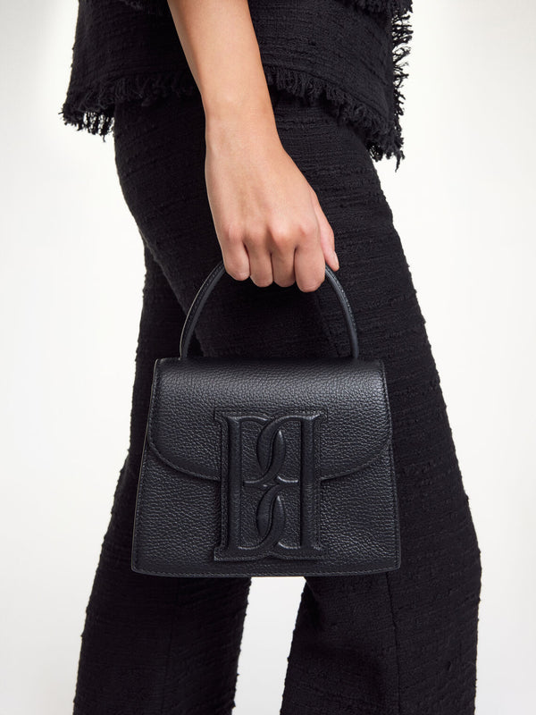 By Malene Birger Ramil veske i strukturert sort skinn, med monogram-motiv i front og justerbar skulderreim.