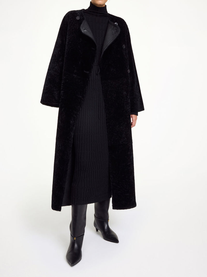 By Malene Birger Sandria lammeskinnskåpe i sort, laget av 100% lammeskinn og pels, med avtagbart belte og maksilengde.