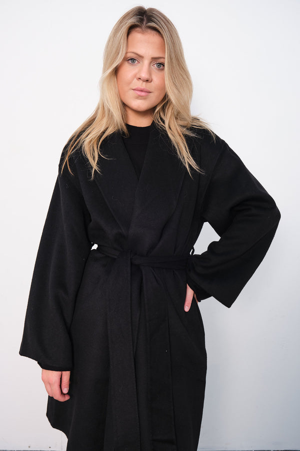 By Malene Birger Trullas kåpe i sort, med en sjal-lignende krage og en rett passform, laget av 100% ull.