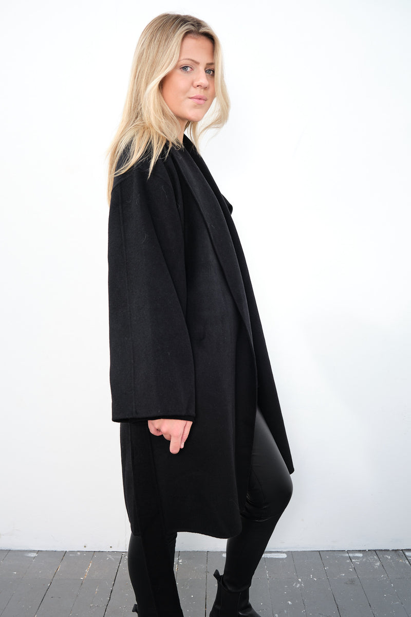 By Malene Birger Trullas kåpe i sort, med en sjal-lignende krage og en rett passform, laget av 100% ull.