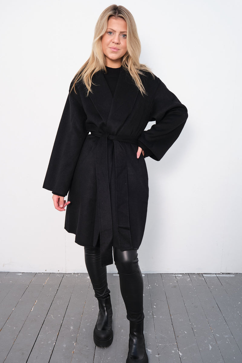 By Malene Birger Trullas kåpe i sort, med en sjal-lignende krage og en rett passform, laget av 100% ull.