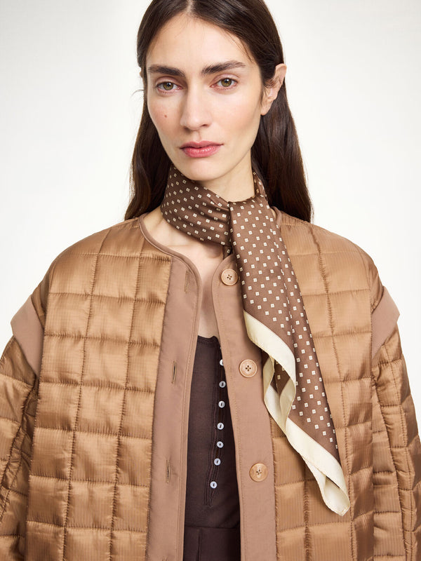 By Malene Birger Velia silkeskjerf i mørkebrun, laget av 100% silke med et elegant mønster og et lite logo i hjørnet.