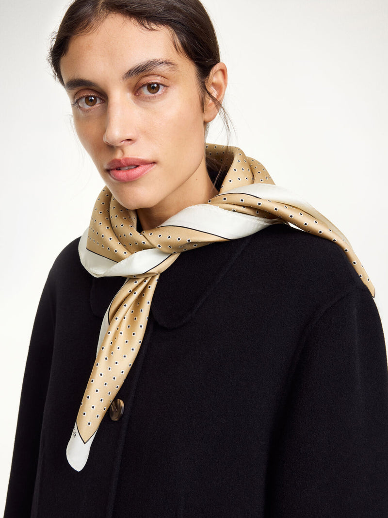 By Malene Birger Velia silkeskjerf i sand, laget av 100% silke med et elegant mønster og et lite logo i hjørnet.