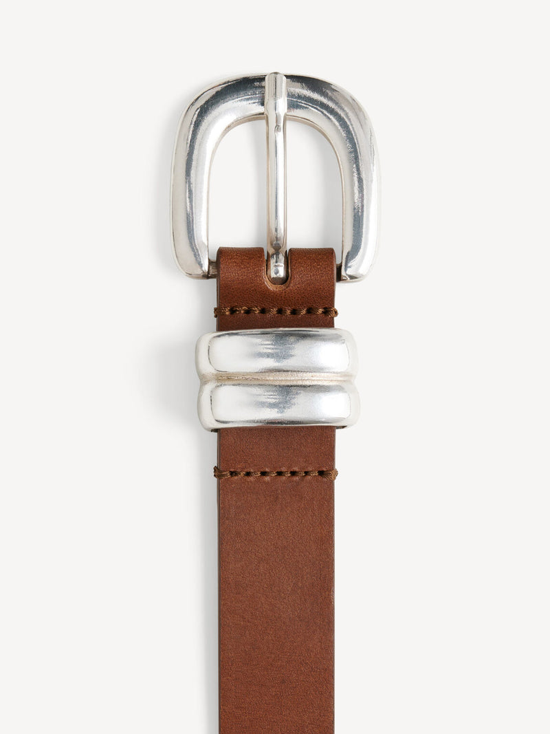 By Malene Birger Zoilo belte i brunt, laget av 100% kuskinn, med en sølvfarget spenne for et røffere uttrykk.